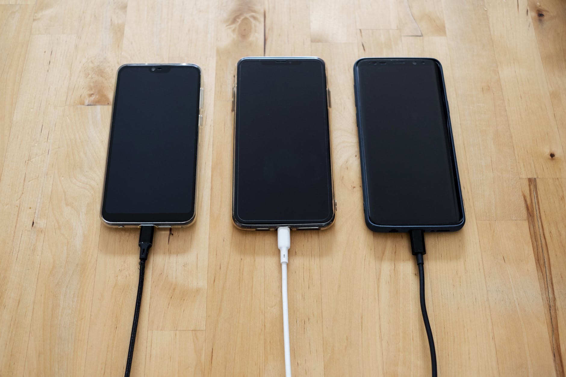 3 smartfony podłączone do ładowarek na biurku
